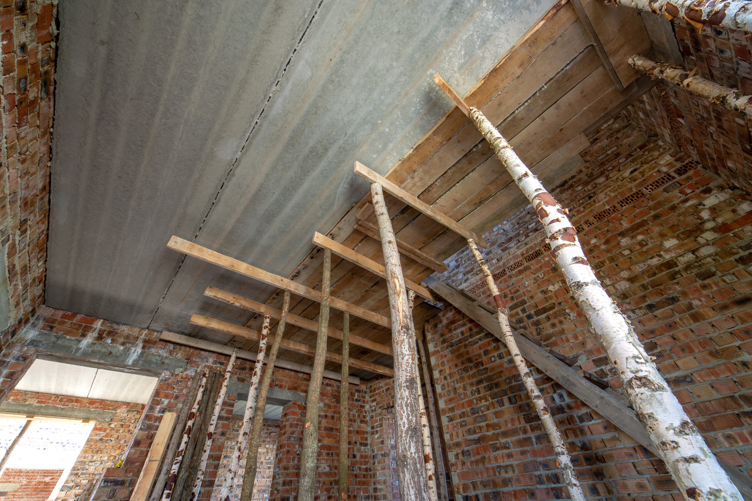 Attic of a building under construction with wooden beams of a roof structure and brick walls.